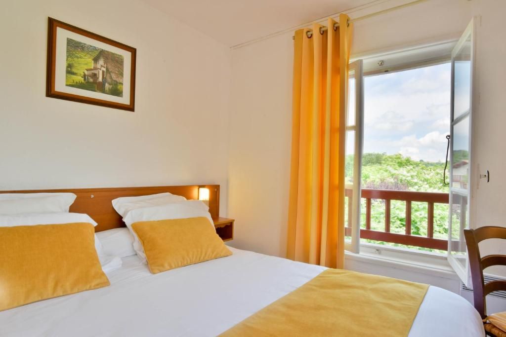 Habitación de hotel con cama, mesita de noche, un cuadro en la pared y un balcón con cortinas amarillas.