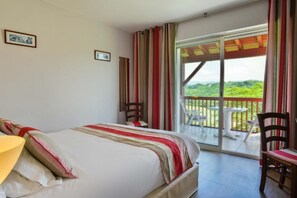 A hotel room with a bed, a chair, a table, and a balcony with a view. - Logis Hotel Baratxartea (Sare)