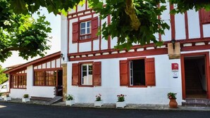 A traditional half-timbered building with red shutters, white walls, and a small porch area with potted plants. - Logis Hotel Baratxartea (Sare)