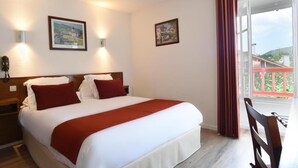 A hotel room with a bed, two wall-mounted lights, two framed pictures, a window with curtains, and a view of a balcony. - Logis Hotel Baratxartea (Sare)
