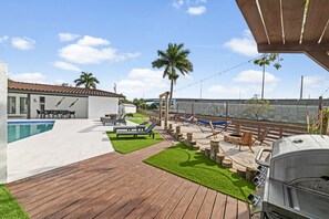 Um quintal com piscina, deck de madeira e área para churrasco.