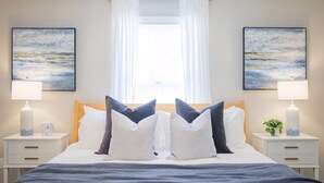 A neatly made bed with a blue blanket, two bedside tables with lamps, and two paintings on the walls.