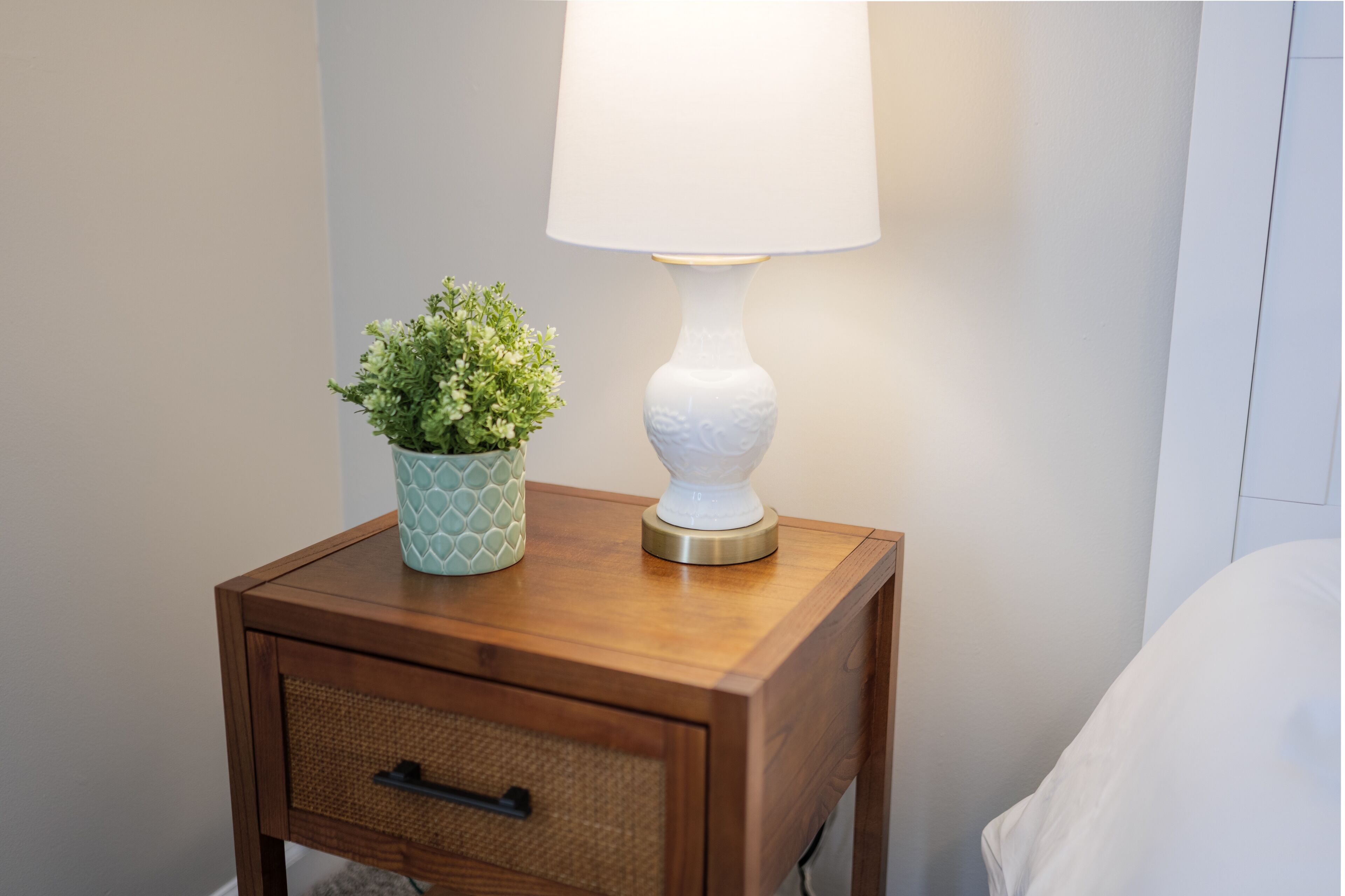 Et natbord i træ med en hvid lampe og en potteplante.