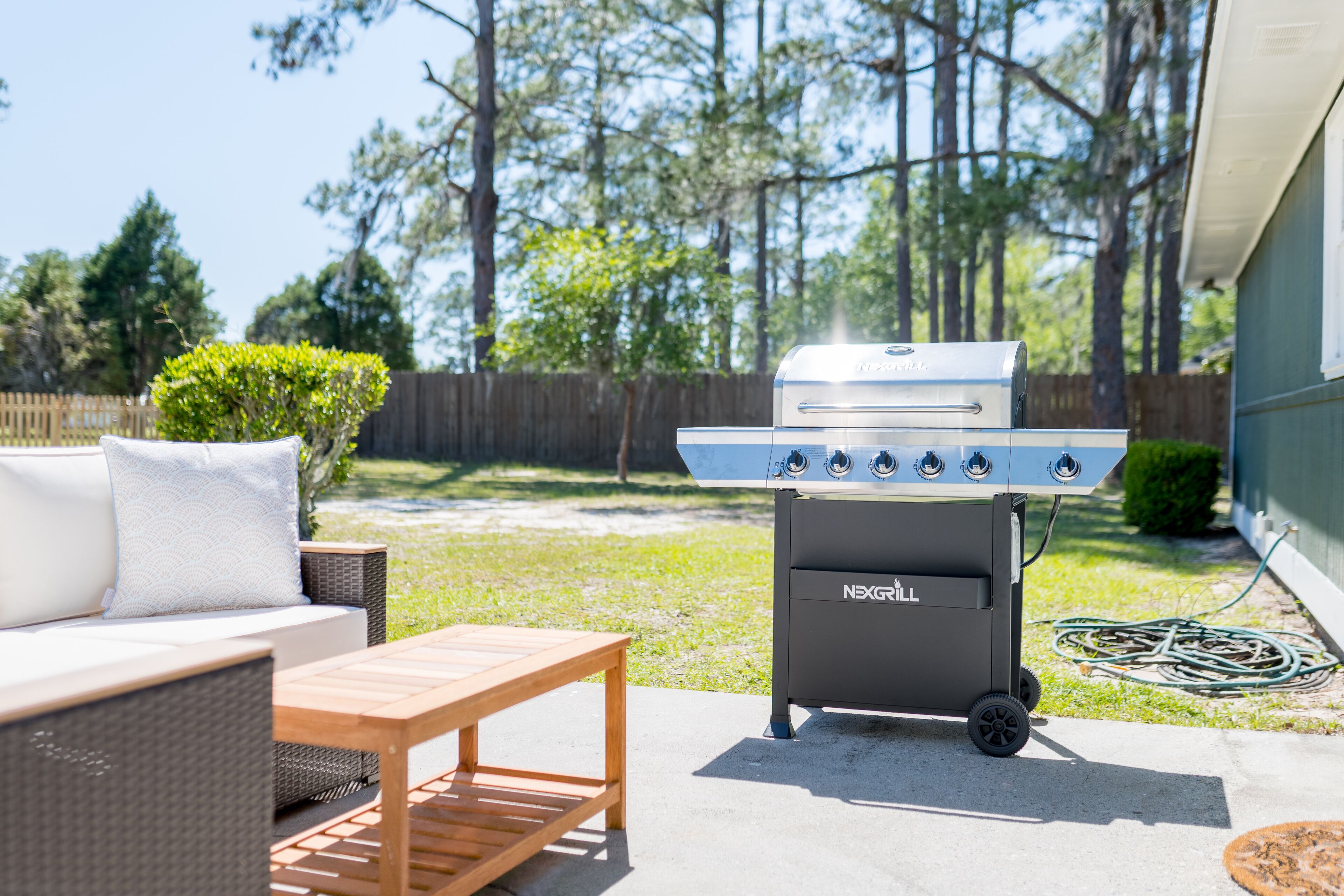 Un patio trasero con una parrilla, un sofá de mimbre y una mesa de madera.