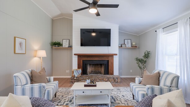 A living room with a fireplace, two sofas, a coffee table, and a television mounted above the fireplace.