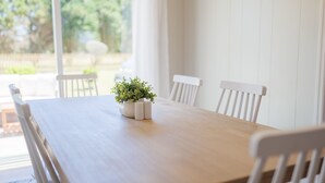 A dining table with white chairs, a potted plant, and a view of greenery outside.