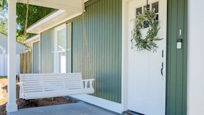 A porch with a white swing, a green door, and a wreath.