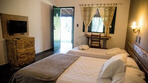 Habitación de hotel con dos camas, un televisor sobre un tocador de madera, una ventana con cortinas y una lámpara fijada a la pared.