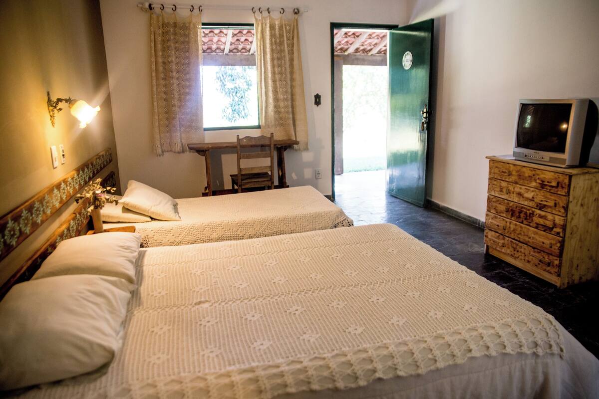 A room with two beds, a wooden dresser, a television, and a window with curtains.