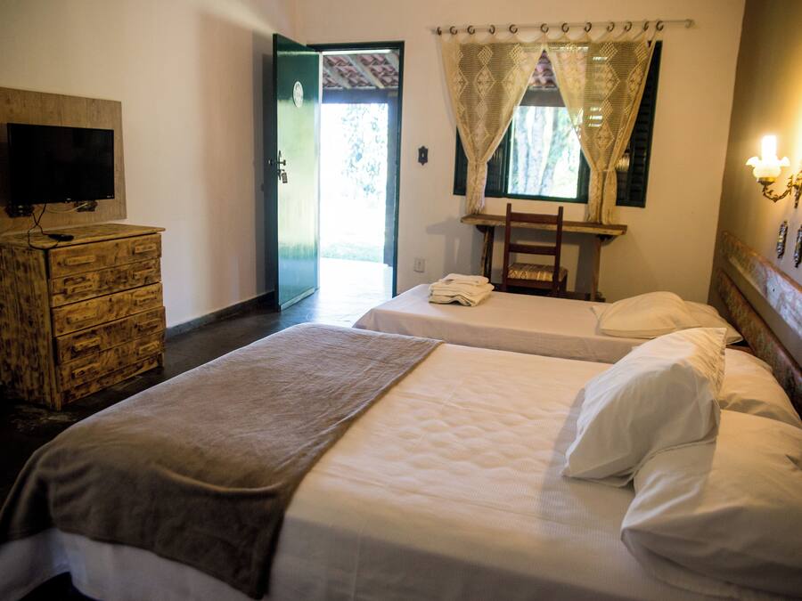 Een hotelkamer met twee bedden, een televisie op een houten dressoir, een raam met gordijnen en een wandlamp.