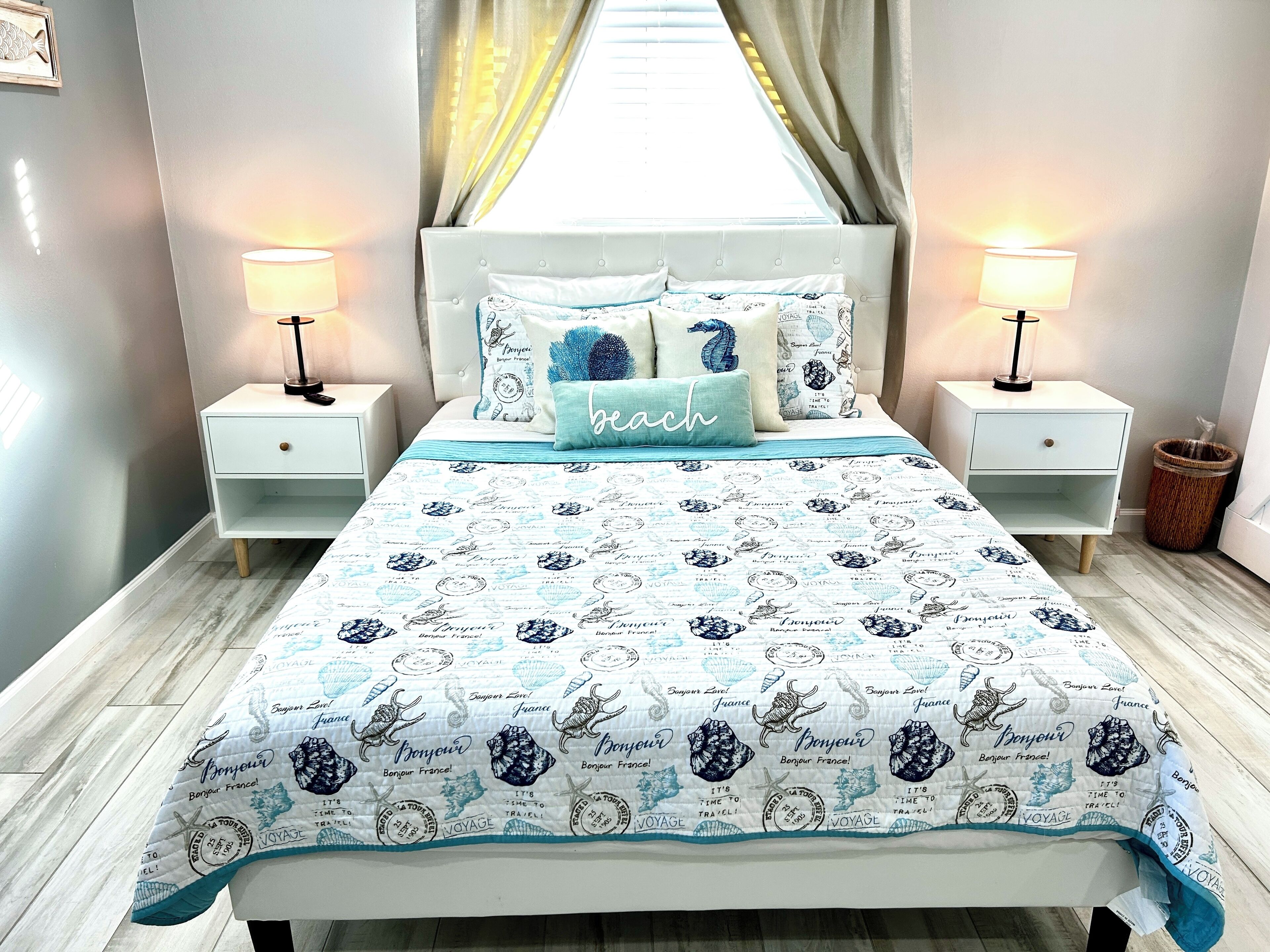 A neatly made bed with a blue and white patterned bedspread, two bedside lamps, and a window with curtains.