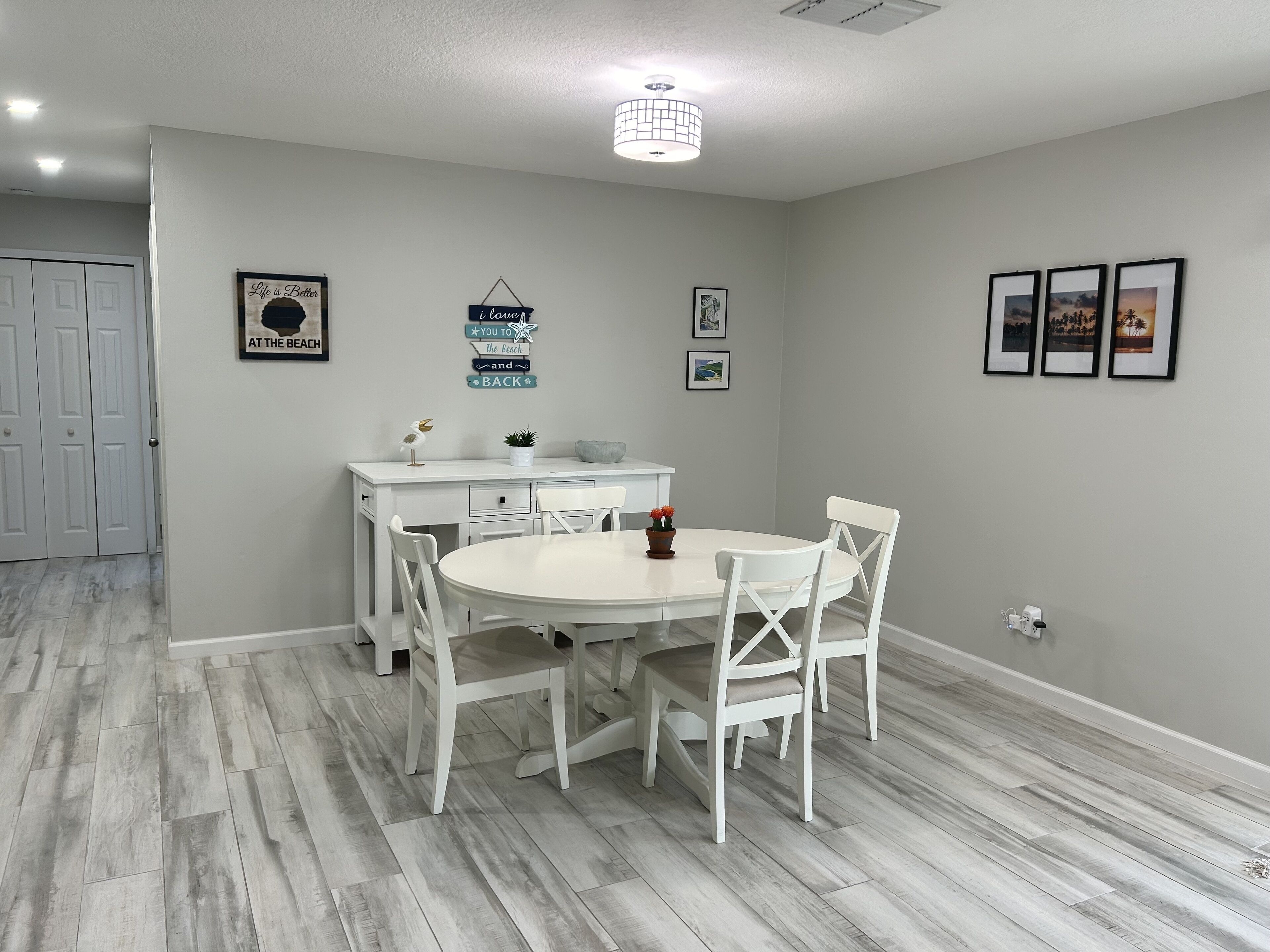 Uma área de refeições com uma mesa e cadeiras brancas, um armário branco e um lustre.