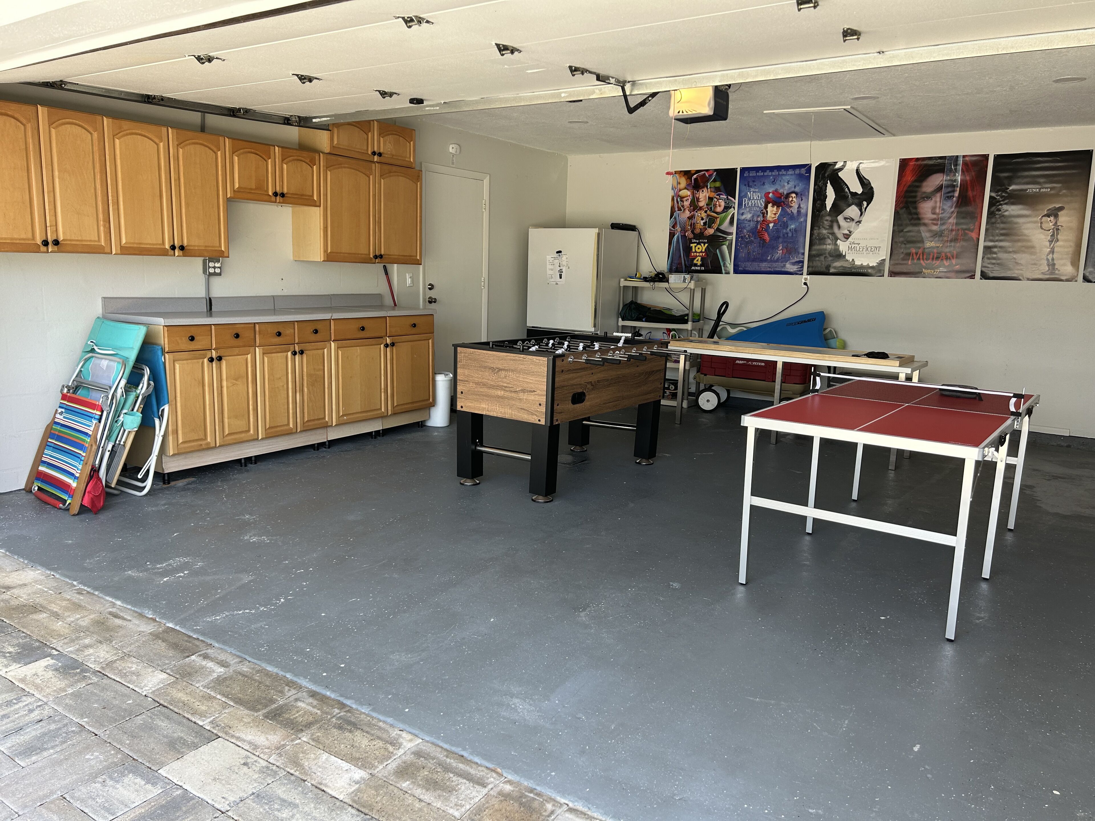 A garage with a foosball table, ping pong table, and wooden cabinets.