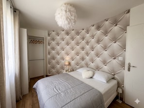 A bedroom with a tufted headboard, a bed with a patterned bedspread, a bedside lamp, and a hanging light fixture. - Caporizon-villa Pommier-6 Personnes-jardin-terrasse-a la Campagne Proche Ville (Sanilhac)