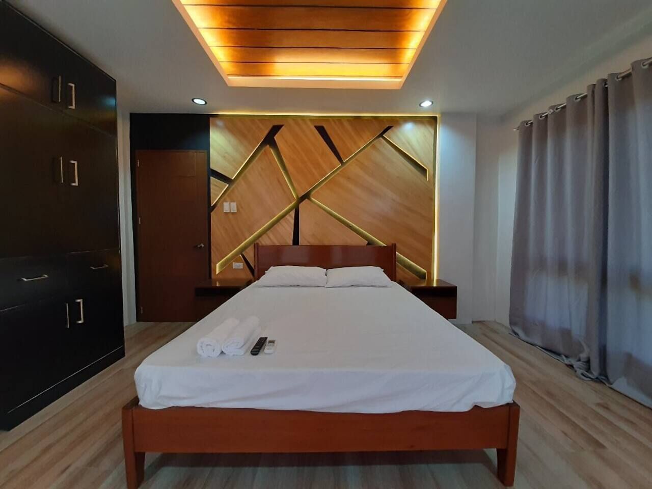 Una habitación de hotel moderna con una cama de madera, cabecera integrada y una lámpara de techo.