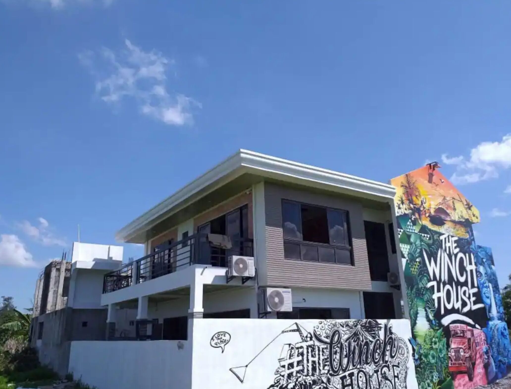Un bâtiment à deux étages, doté d’un balcon à l’étage supérieur, d’une grande fresque sur le côté et d’un climatiseur sur le toit.