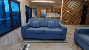 Ein modernes Wohnzimmer mit einem blauen Sofa, einem Couchtisch und Blick auf eine Küche und einen Essbereich.