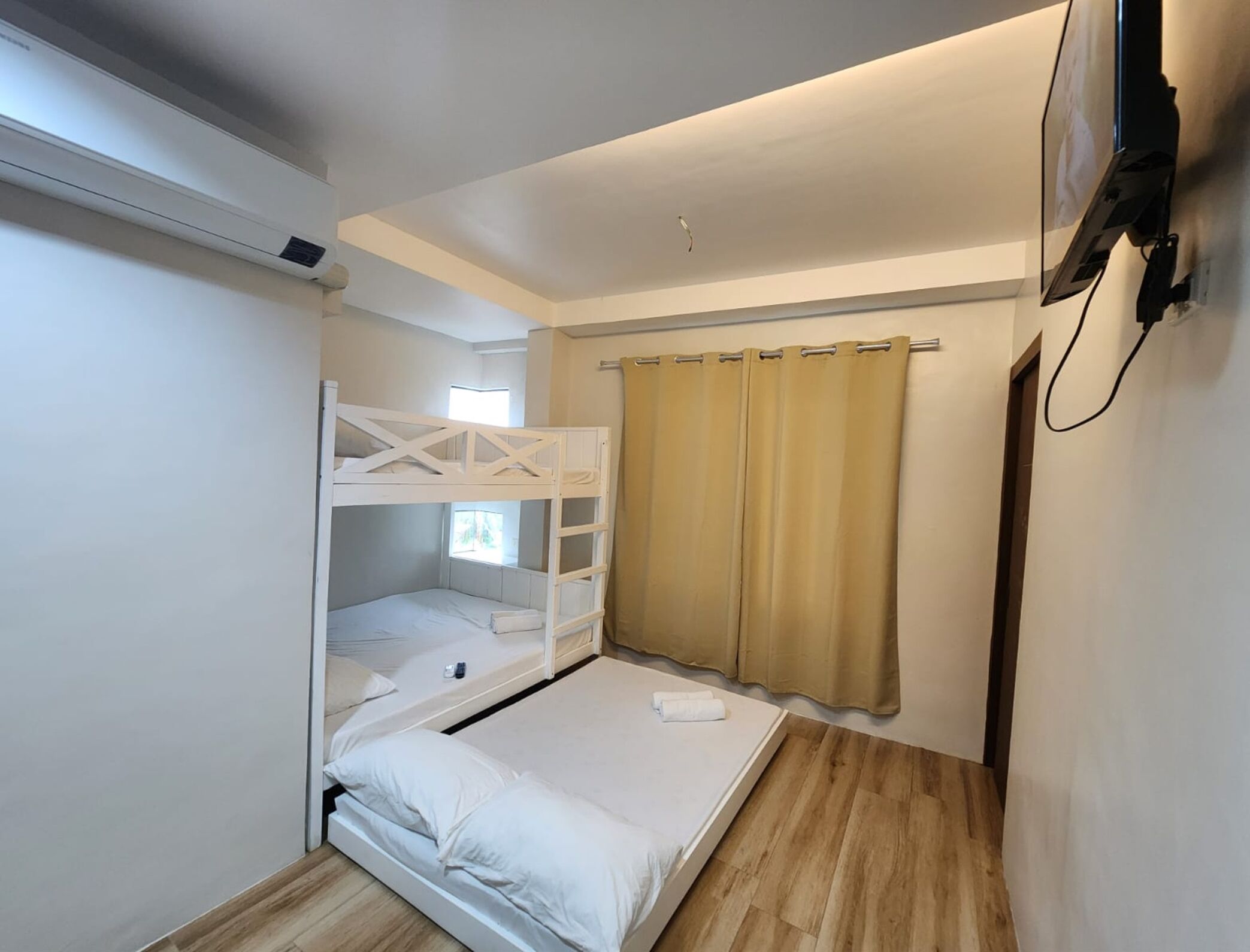 A compact room with a bunk bed, a single bed, a window, and a curtain.