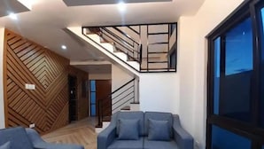 Ein modernes Wohnzimmer mit einem blauen Sofa, einer Wandpaneinung aus Holz und einer Treppe, die in eine obere Ebene führt.
