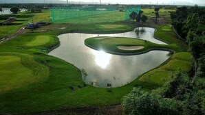 Ein Golfplatz mit mehreren Teichen und Grünflächen, umgeben von Bäumen und Bergen in der Ferne.