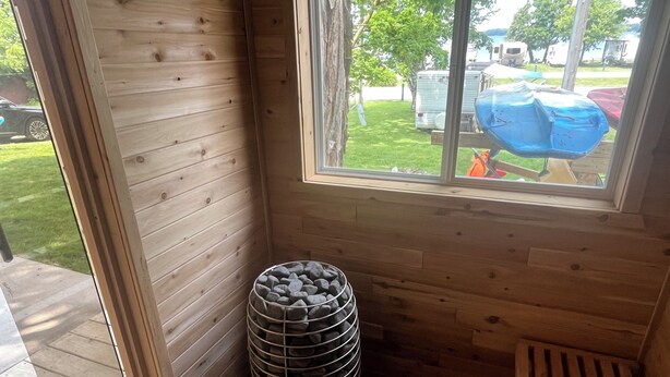 Interior de una cabaña de madera con ventana, una cesta metálica y un banco.
