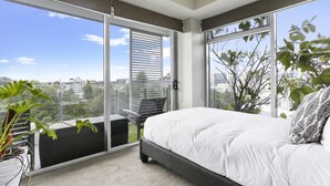Ein Schlafzimmer mit einem großen Bett, einer Schiebetür zu einem Balkon und Blick auf die Stadtlandschaft.