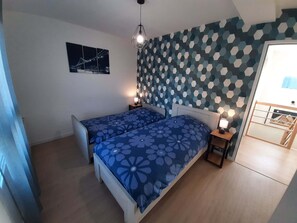 Een slaapkamer met twee bedden, een wand met een geometrisch patroon, een ingelijst schilderij en een houten hoofdbord.