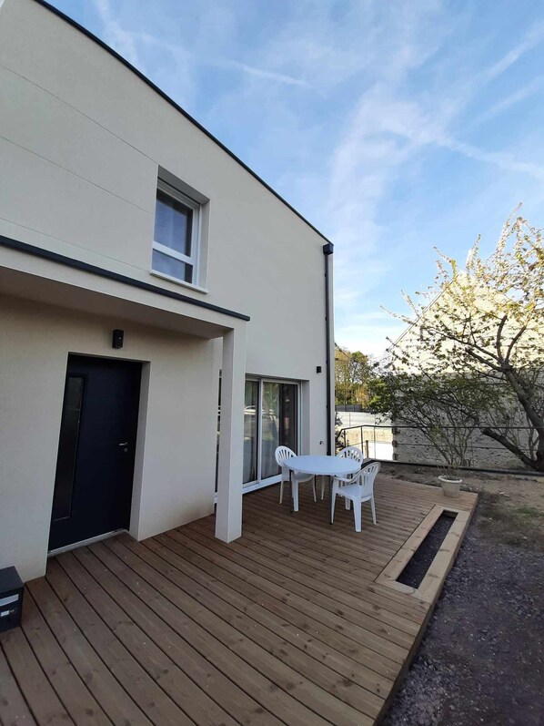 Een modern gebouw met een houten terras, een witte tafel en stoelen, en een zwarte deur.