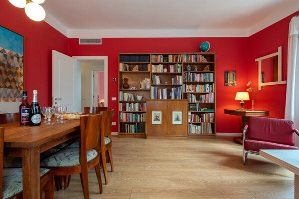 Une pièce avec une table à manger en bois, des chaises, une bibliothèque et un mur rouge.