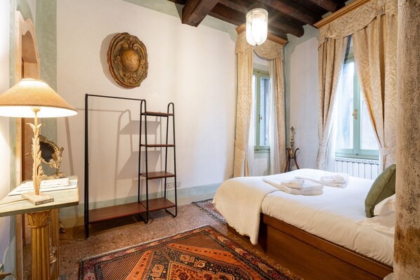 A bedroom with a wooden bed, a nightstand with a lamp, a decorative mirror, and a patterned rug. - two bedrooms apartment in San Marco (Venezia)