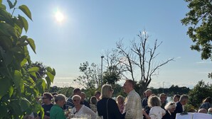 En grupp människor hade samlats runt en bardisk av trä, med vinflaskor och glas, en gitarr och ett notställ med noter.