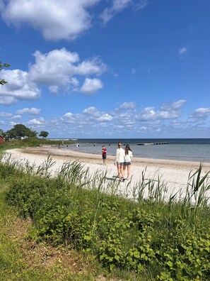 A beach with a sandy shore, grassy areas, and a clear blue sky with clouds. - Borgvik Gotland  (Katthammarsvik)