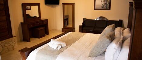 A hotel room with a large bed, a wooden dresser, a mirror, a television, and a framed picture on the wall.