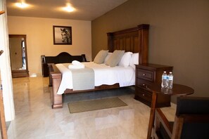 A bedroom with a large bed, wooden headboard, bedside tables, a small round table with water bottles, and a framed picture on the wall. - Sacramento Hotel Boutique  (Ezequiel Montes)