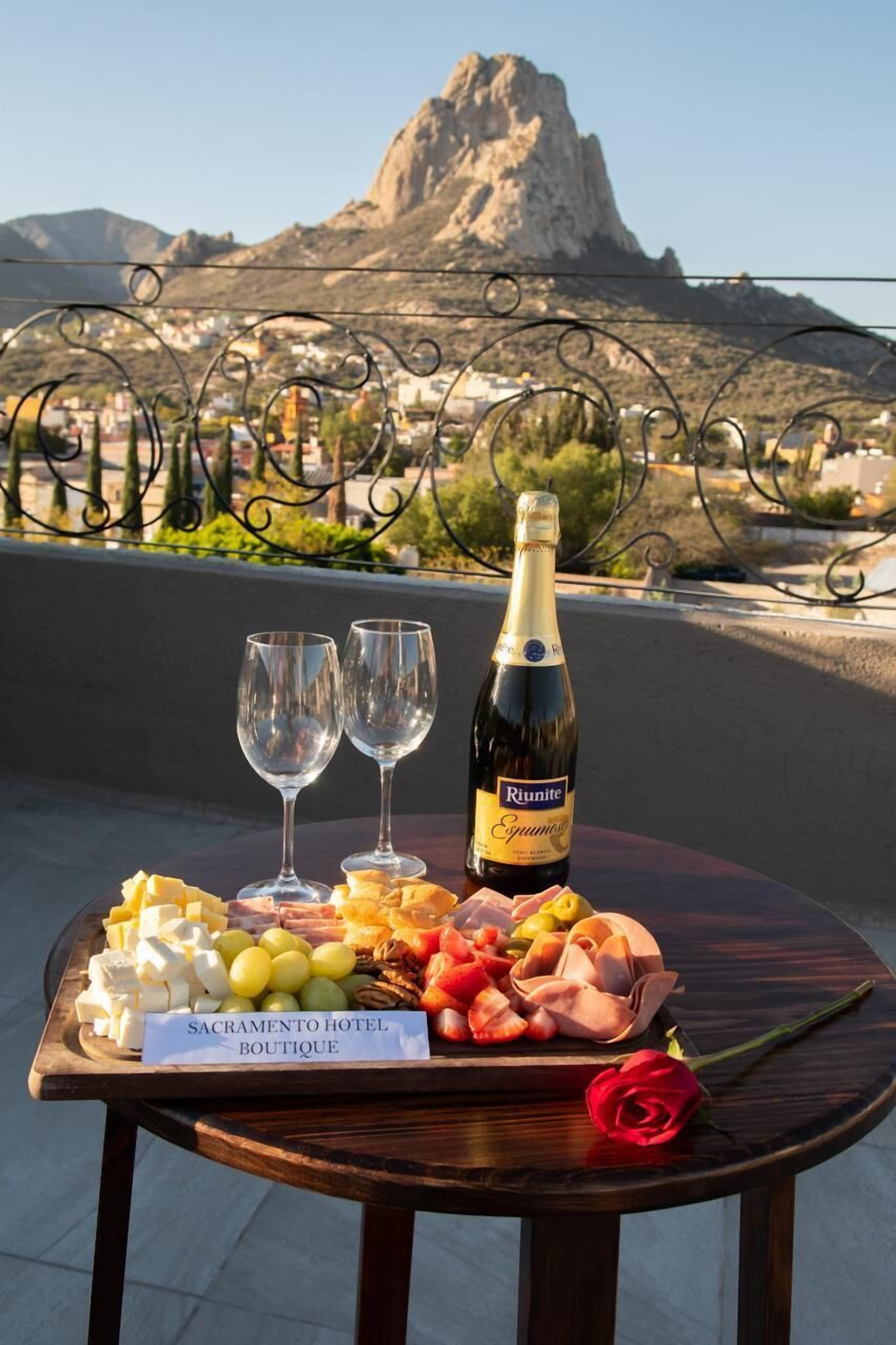 A table with a bottle of Riunite, two glasses, and a variety of cheeses and meats on a wooden table with a sign reading "Sacramento Hotel Boutique".