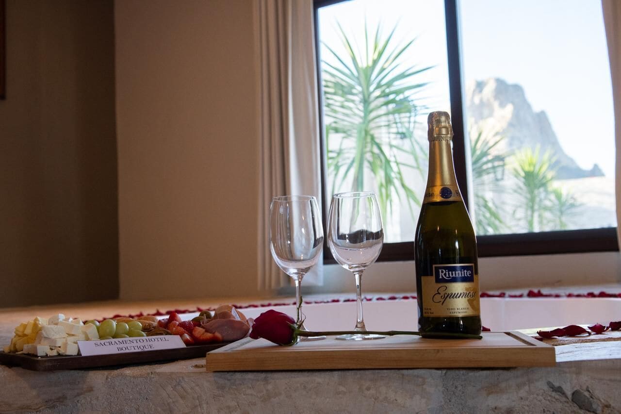 Una botella de vino espumoso Riunite, dos copas de vino vacías y un plato con quesos y frutas variadas sobre una tabla de madera.