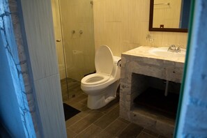 A bathroom with a white toilet, a stone sink vanity, and a glass shower enclosure. - Sacramento Hotel Boutique  (Ezequiel Montes)