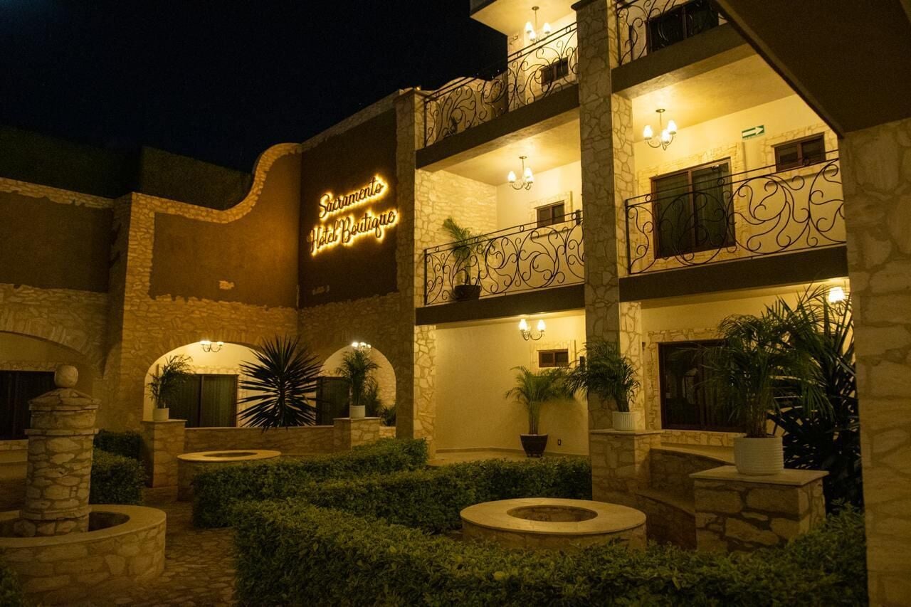 A multi-story building with a stone facade, outdoor seating areas, and a neon sign for a boutique hotel.