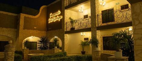 A multi-story building with a stone facade, outdoor seating areas, and a neon sign for a boutique hotel.