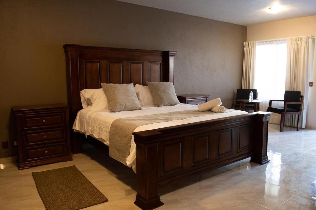 A bedroom with a large wooden bed, a nightstand, a dresser, a desk, and a chair.