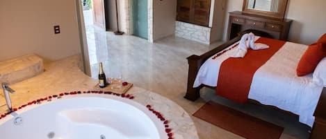 A bedroom with a large bathtub, a bed with a red blanket, and a wooden dresser.