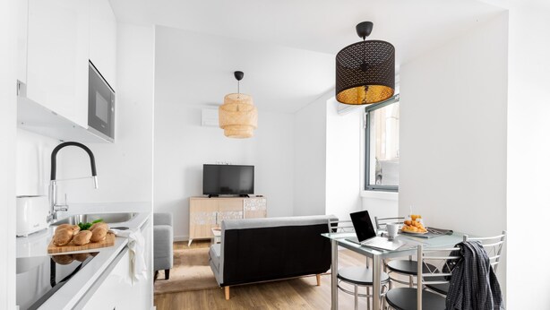 A modern kitchen with a built-in oven, a dining area with a glass table and chairs, and a black sofa. - Estrela Delight by Homing (Lisbon)