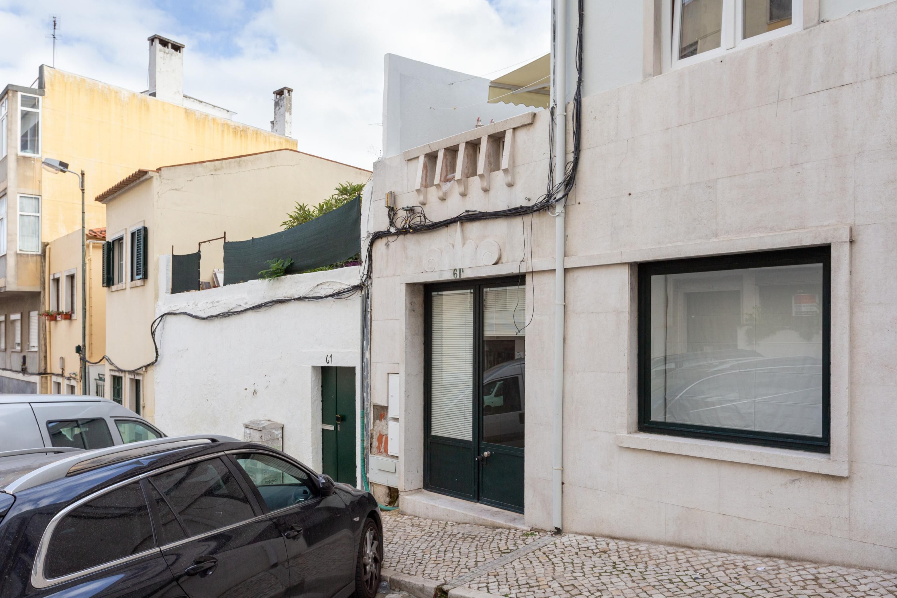 A modern building with a large window and a door, a car parked in front, and a cobblestone street.