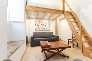 A room with a wooden staircase, a grey sofa, a wooden coffee table, and a colorful abstract painting on the wall.