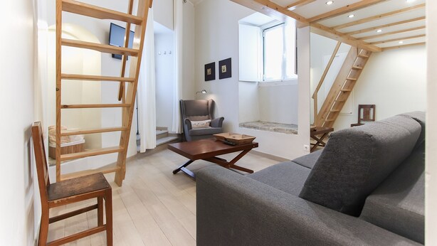 A loft-style room with a wooden ceiling, a gray sofa, a wooden ladder, a chair, and a small table. - Santa Catarina Harmony by Homing (Lisbon)