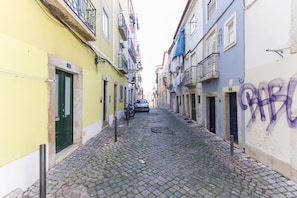 A narrow cobblestone street flanked by buildings with balconies and a parked car.