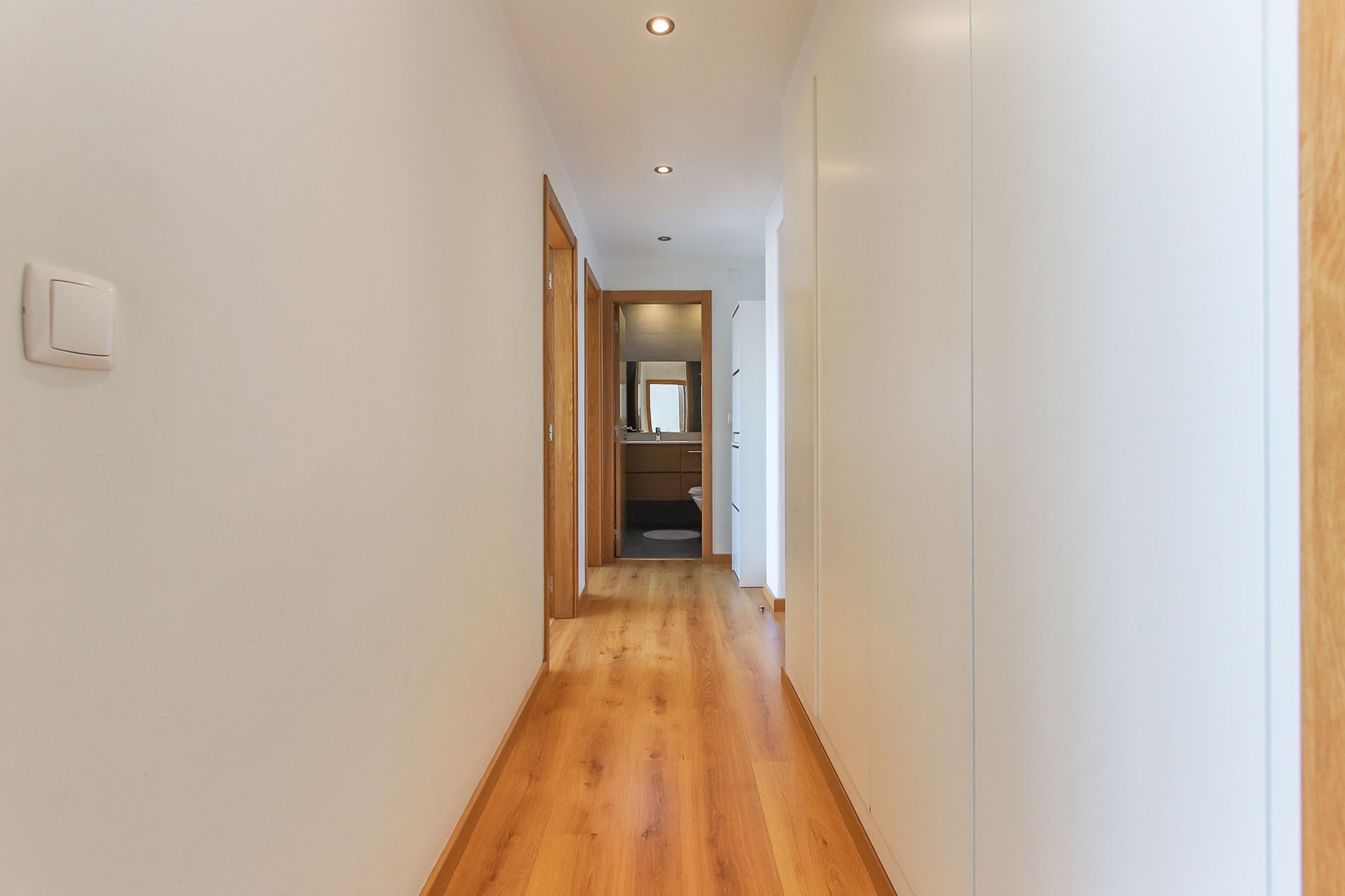 A narrow hallway with wooden flooring and white walls.