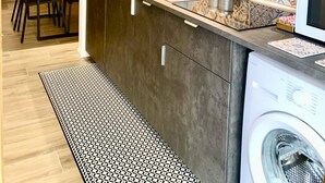 Cozinha moderna com armários escuros, painel decorativo atrás do fogão, micro-ondas embutido e máquina de lavar roupa.