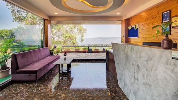A modern reception area with a marble reception desk, a purple sofa, and a view of the outdoors. - Harmony Palace (Mahabaleshwar)
