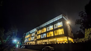 A multi-story building with balconies and air conditioning units, a car parked in front, and a well-lit entrance. - Harmony Palace (Mahabaleshwar)